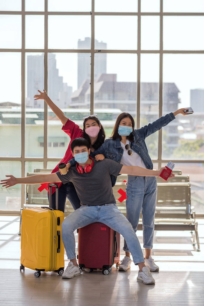 Portrait of happy Asian friends wearing protective mask with luggage at airport terminal. Photo shoot and wait for departure of holiday vacation during covid-19 omicron pandemic. - Photo, image