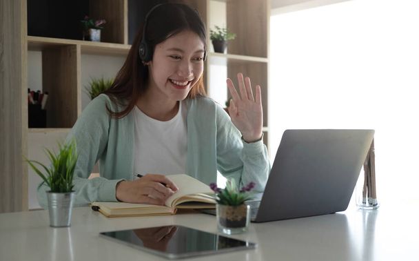 An Asian student in casual clothes is greeting her friend at a video conference. During the time of studying online at hom - Photo, image