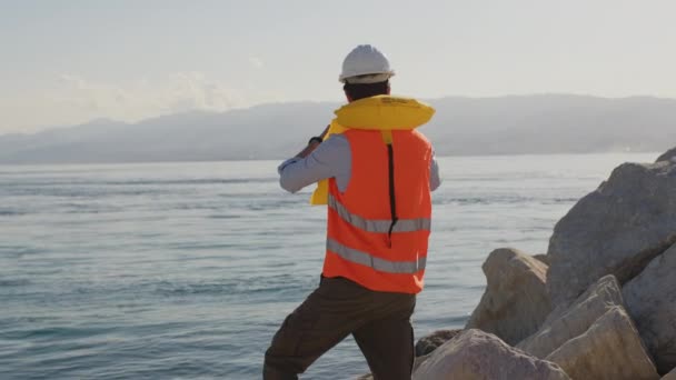 Joven ingeniero naval controla el mar desde el puerto con prismáticos - Metraje, vídeo
