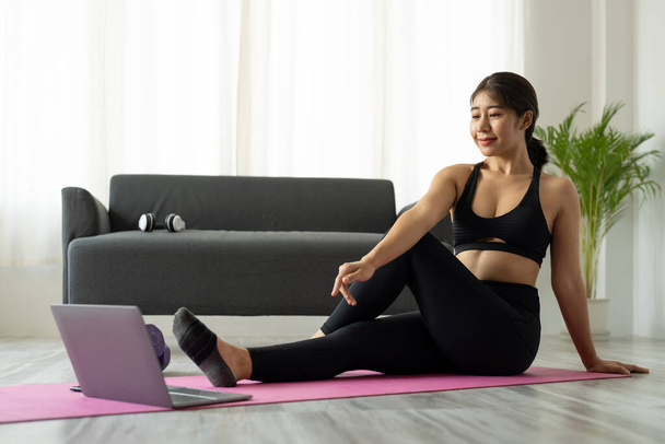 Fit sportos fiatal ázsiai nő online edzés gyakorlat otthon. Aktív egészséges lány élvezni sport pilates jóga fitness edzés laptop számítógép nyújtás jóga matrac videó osztály - Fotó, kép