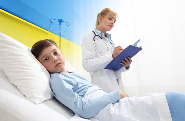 Humanitarian Aid, help for medical protection for Ukraine war. Doctor and sick child in hospital bed. Boy looking at camera. Yellow and blue colors of the flag of Ukraine. Injured Ukrainian refugees - Foto, Imagen