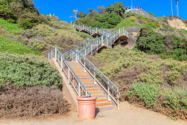 Staircase on a slope of a mountain at San Clemente, California. Stairs with ornate tile risers and metal handrails in the middle of wild shrubs and trees on the slope. - Photo, Image