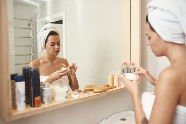 Woman taking cream from container in bathroom - Valokuva, kuva