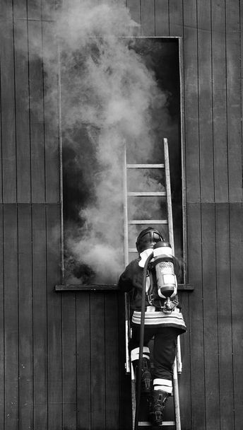 pompier en action dans la caserne de pompiers avec un appareil respiratoire autonome et un cylindre à oxygène et la fumée épaisse qui sort de la fenêtre - Photo, image