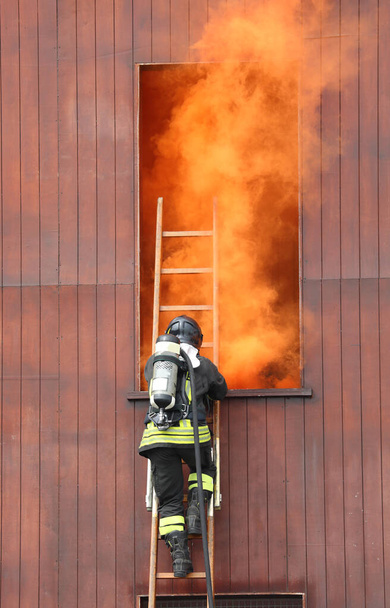 hasič v akci na hasičské stanici se samostatným dýchacím přístrojem a kyslíkovými bombami během záchranného cvičení a hustým oranžovým kouřem vycházejícím z okna - Fotografie, Obrázek