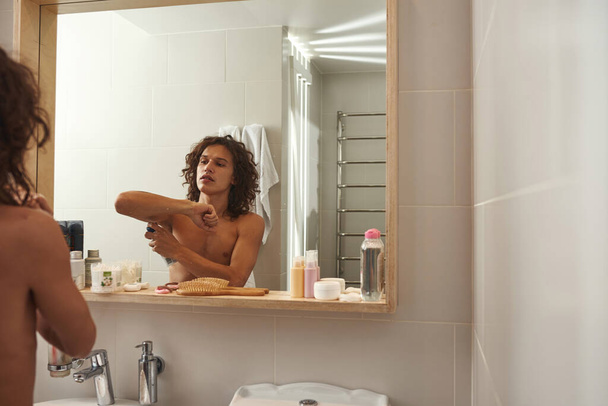 Man apply antiperspirant on his armpit in bathroom - Photo, image