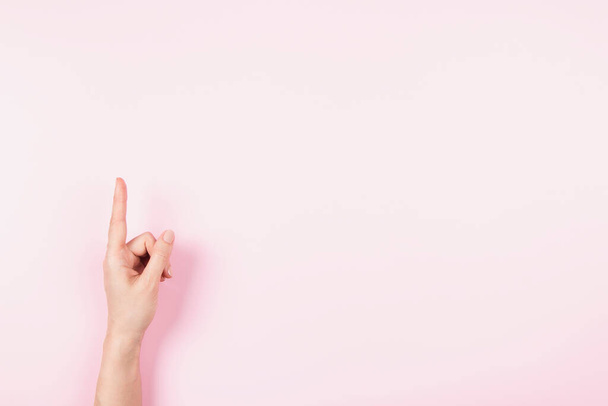 Kobieta wskazując palcem wskazującym na coś wirtualnego i niewidzialnego, skopiuj miejsce na pastelowym różowym tle. Gest ręki, numer jeden. - Zdjęcie, obraz