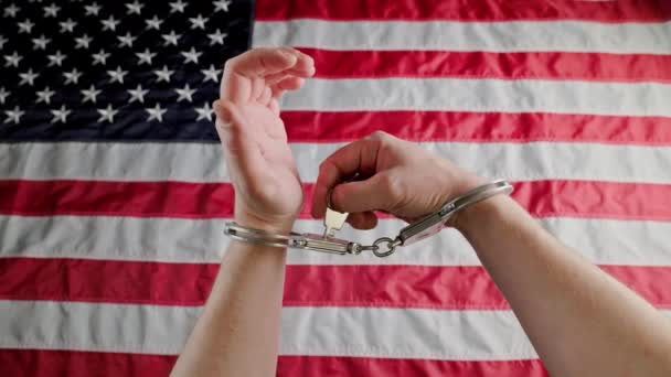 hands in handcuffs against the US flag unlocking handcuffs and putting them off - Séquence, vidéo
