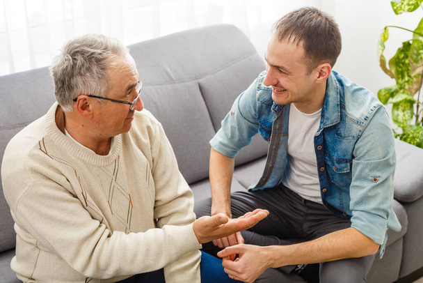fröhlicher Rentner und erwachsener Sohn reden zu Hause - Foto, Bild