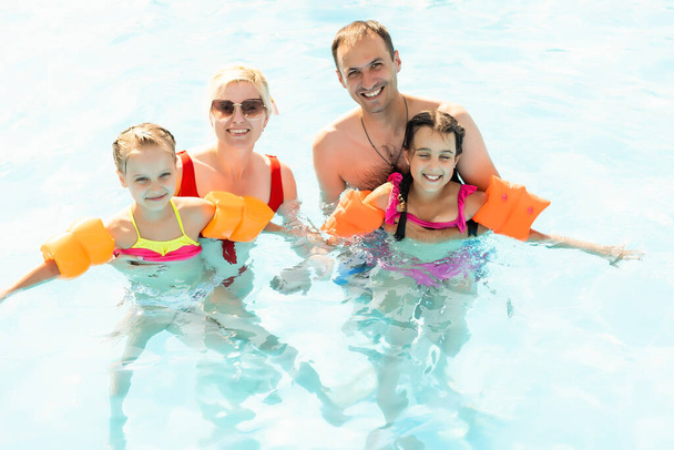Χαρούμενη οικογένεια που διασκεδάζει στις καλοκαιρινές διακοπές, παίζει στην πισίνα. Έννοια ενεργού υγιεινού τρόπου ζωής - Φωτογραφία, εικόνα