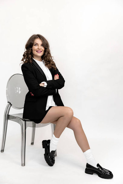 beautiful young woman in black suit sitting on the chair in white studio  - Foto, Bild