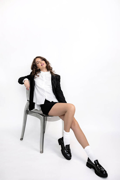 beautiful young woman in black suit sitting on the chair in white studio  - Valokuva, kuva