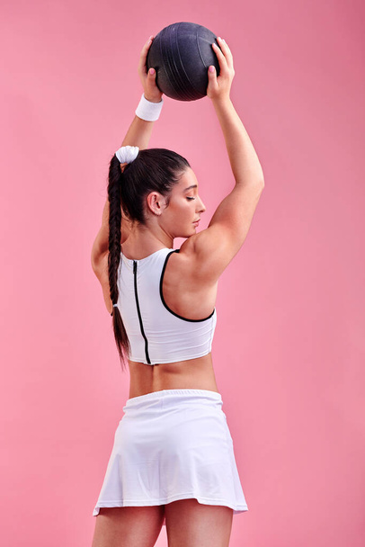 Постійно високий і сильний. Студійний знімок спортивної молодої жінки, що тримає м'яч над головою на рожевому фоні
. - Фото, зображення