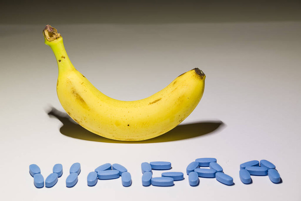 Plátano amarillo ascendente con la palabra "viagra" hecha con píldoras de erección azul, concepto de solutione a problemas masculinos - Foto, imagen