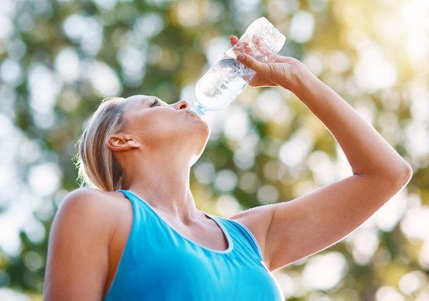 Vždy zůstat hydratovaný během tréninku. Nízký úhel záběr dospělé ženy pitné vody z láhve venku. - Fotografie, Obrázek