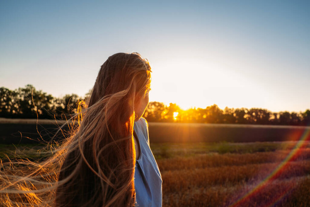 Peaceful woman with long hair in blue linen dress spending time in nature on summer day in sunset. Stress and psychological resilience. Spend Time in Nature to Reduce Stress and Anxiety - Photo, Image