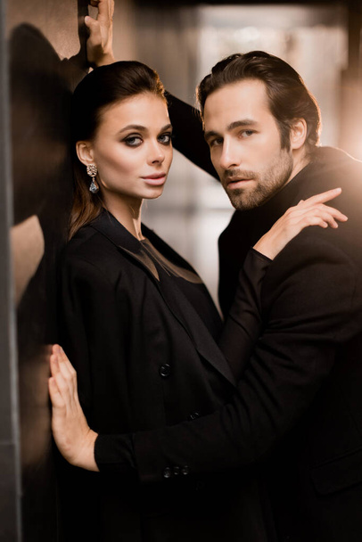 Stylish dressed caucasian couple having a photoshoot for magazine cover in black outfits. Beautiful young woman with charming beard man posing at the camera, fashion models concept.  - Photo, Image