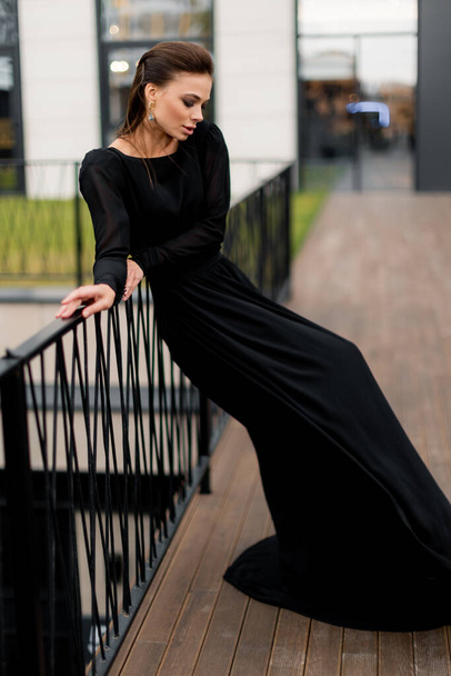 Gorgeous woman in stylish black dress posing for the photo, showing self confidence. Beautiful female working as fashion model, having a photoshoot for magazine cover. - Foto, Imagen