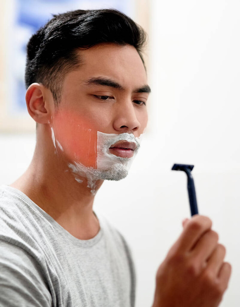 I really need to replace this. Shot of a young man at home getting razor burn on his face from shaving with a disposable razor. - Photo, Image