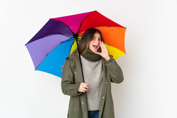 Young caucasian woman holding an umbrella isolated on white background shouting with mouth wide open - Foto, Imagem