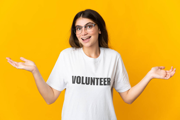 Giovane donna volontaria isolata su sfondo giallo con espressione facciale scioccata - Foto, immagini