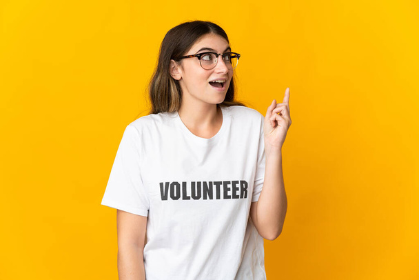 Mladá dobrovolnice izolovaná na žlutém pozadí přemýšlí o nápadu ukazovat prstem nahoru - Fotografie, Obrázek