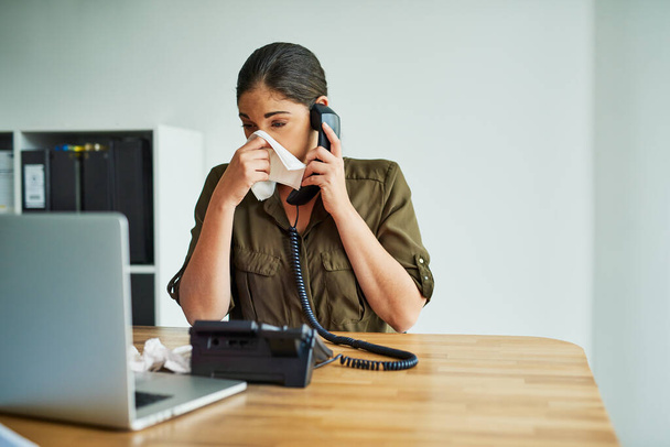 Es ist ein unerträglicher Zustand, in dem zu arbeiten. Aufnahme einer jungen Geschäftsfrau, die sich beim Telefonieren in einem Büro die Nase pustet. - Foto, Bild
