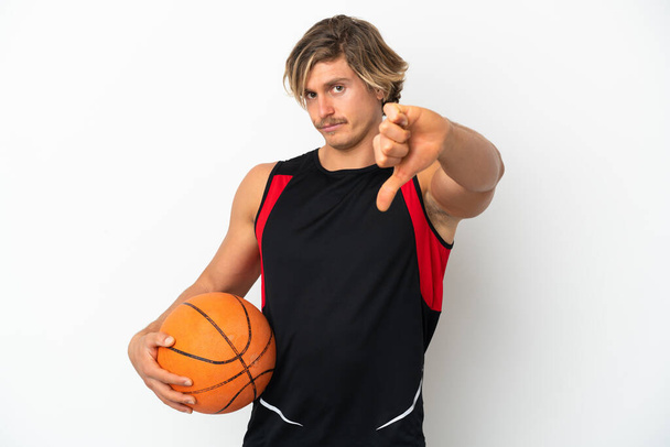 Joven hombre rubio sosteniendo una pelota de baloncesto aislado sobre fondo blanco mostrando el pulgar hacia abajo con expresión negativa - Foto, imagen