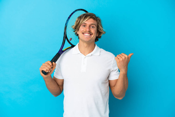 giocatore di tennis biondo uomo isolato su sfondo blu che punta verso il lato per presentare un prodotto - Foto, immagini