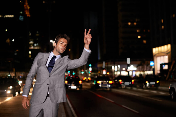 Taxi. A handsome businessman hailing a cab while standing in a busy city street at night. - Foto, imagen