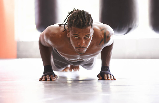 Molding his body into a fighting machine. Portrait of a young boxer doing pushups in a gym. - Foto, Imagen