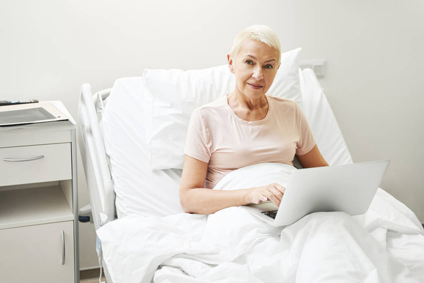 Elderly woman working on laptop from hospital - Zdjęcie, obraz