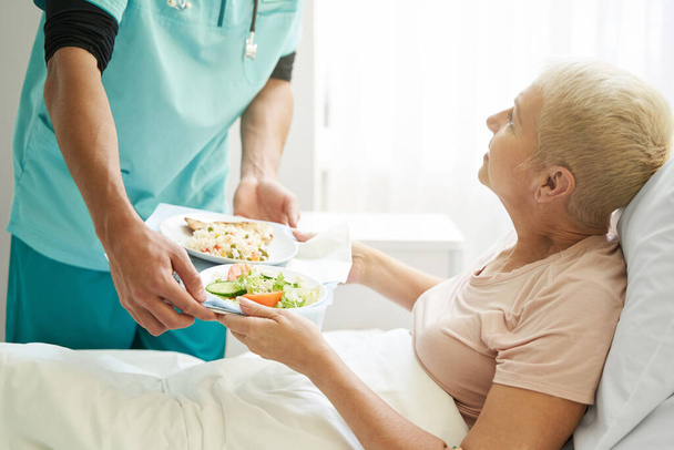 Old female taking breakfast from worker of hospital - Photo, Image