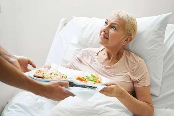 Aging lady getting meal tray from hospital employee - Zdjęcie, obraz