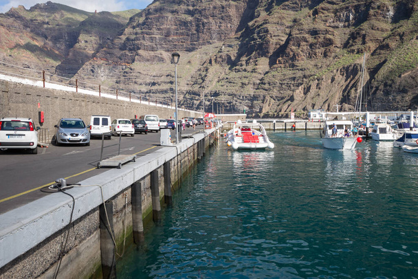 Los Gigantes İskelesi, yolda park etmiş arabalar, bataklıklara yanaşmış eğlence tekneleri ve arka planda Los Gigantes uçurumu. Tenerife, Kanarya Adaları. İspanya - Fotoğraf, Görsel