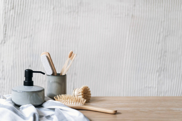 Morning routine concepts. Close up view of ceramic cup with toothbrush on wooden shelf in bathroom with soap dispenser, towel and hair brush. Personal accessories for self care against copy space wall - Photo, Image
