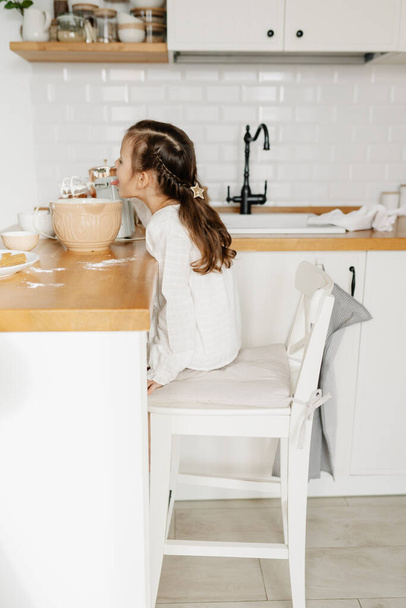 Little Caucasian brown-haired girl baking on white kitchen at home - Foto, Bild