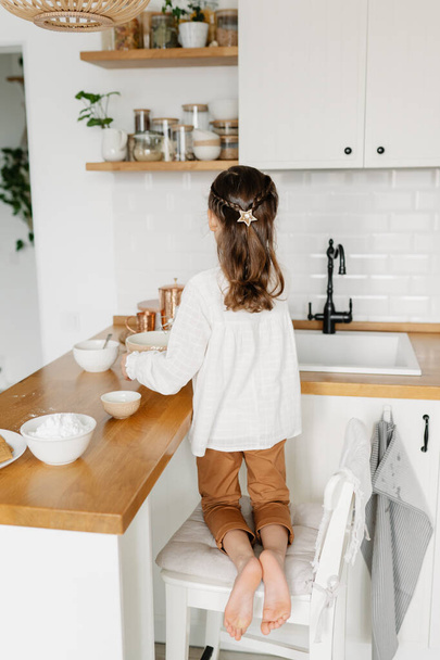 Little Caucasian brown-haired girl baking on white kitchen at home - Фото, изображение