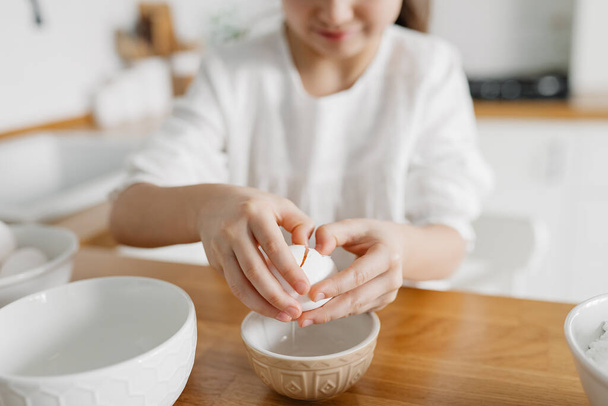 Pieni valkoihoinen ruskeahiuksinen tyttö leipoo valkoisessa keittiössä kotona - Valokuva, kuva