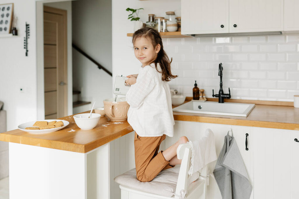 Little Caucasian brown-haired girl baking on white kitchen at home - Фото, изображение