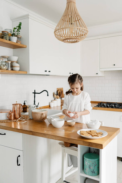 Little Caucasian brown-haired girl baking on white kitchen at home - Valokuva, kuva