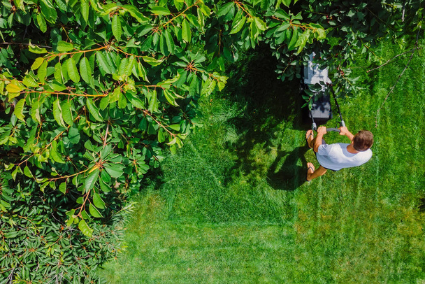 Gardener pushing lawn mower for cutting green grass in garden at summer. Aerial view. - 写真・画像