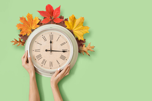 Female hands with clock and autumn leaves on color background. Daylight saving time - Foto, Imagem