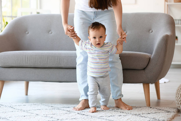 Little baby boy learning to walk with his mother's help at home - 写真・画像