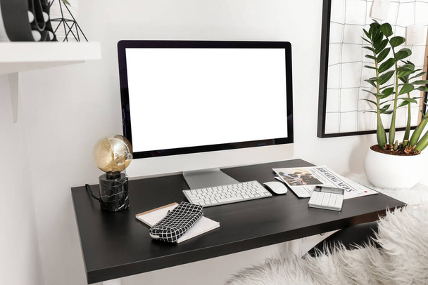 Modern computer, lamp and stationery on table near light wall - Photo, Image