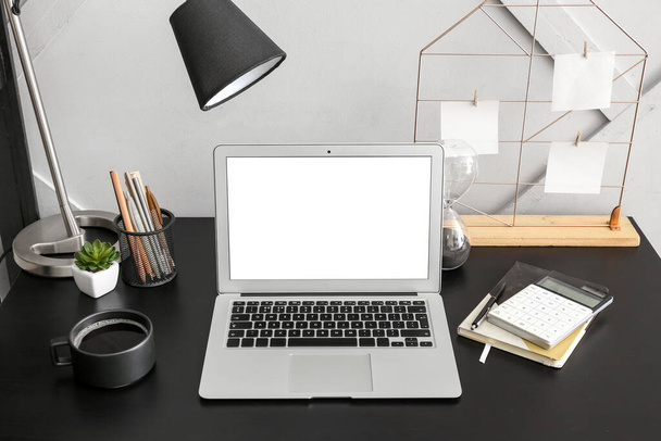 Современный ноутбук, лампа, канцелярские принадлежности и чашка кофе на столе - Фото, изображение