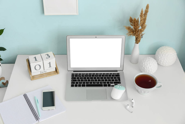 Сучасний ноутбук, мобільний телефон, календар і чашка з чаєм на столі біля кольорової стіни
 - Фото, зображення