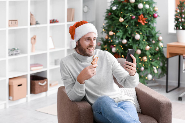 Jongeman in kerstmuts met kerstkoekje neemt selfie thuis - Foto, afbeelding
