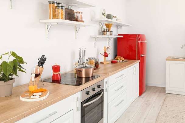 Interior de cocina ligera con nevera roja, mostradores y estantes - Foto, Imagen