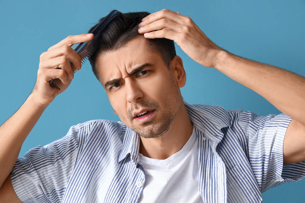 Worried young man combing hair on blue background, closeup - Foto, Bild